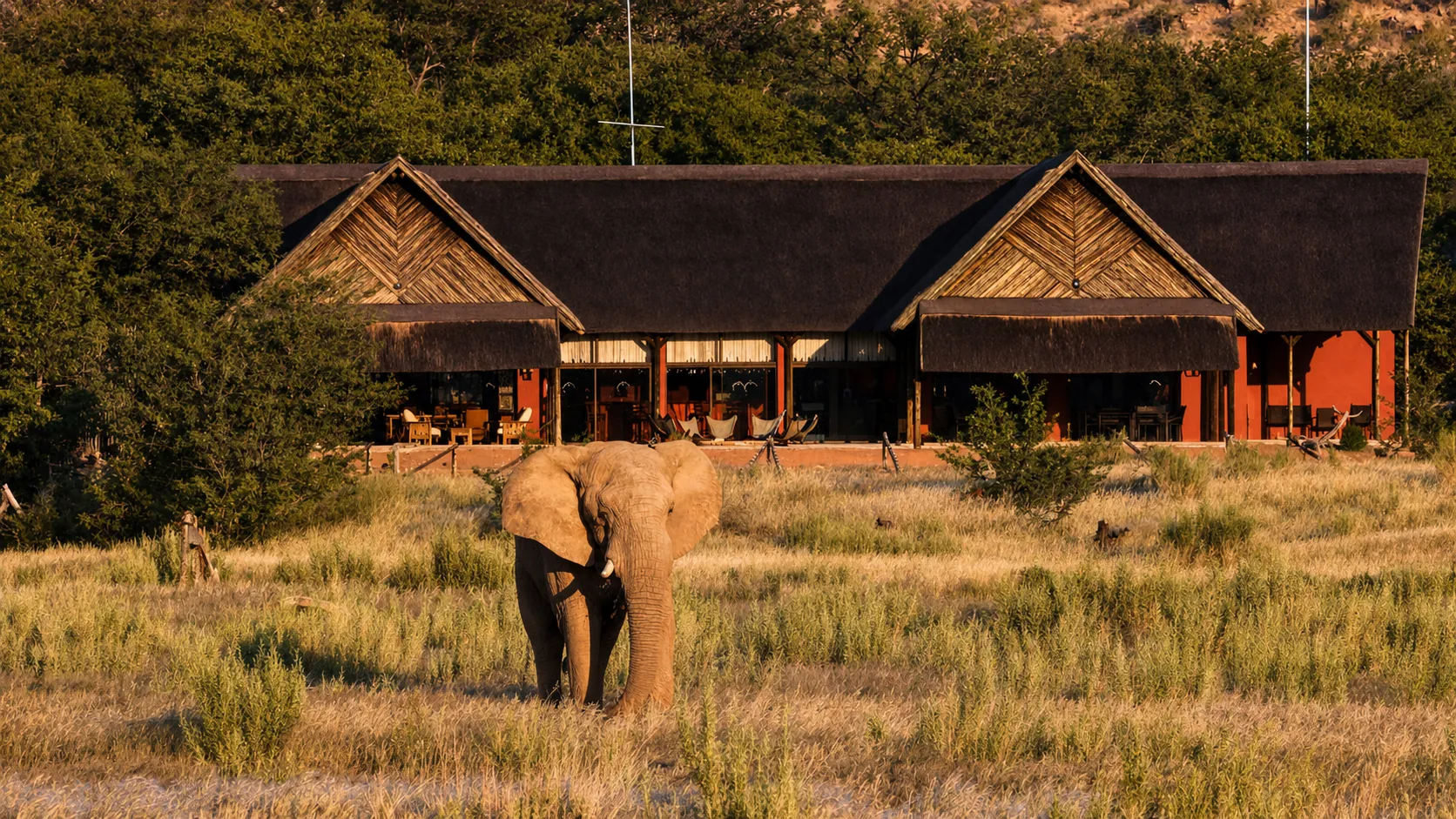 Guests around the fire pit at Hobatere Lodge at dusk, with the hills of the concession and an open sunset sky beyond.