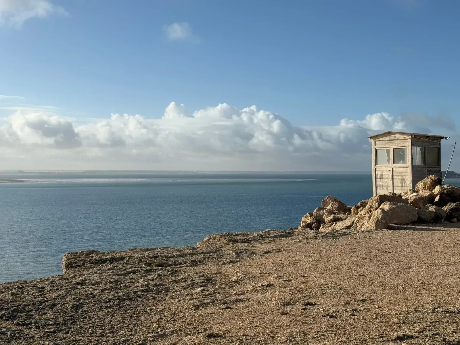 A weathered wooden lookout hut on a rocky point above still, glassy water