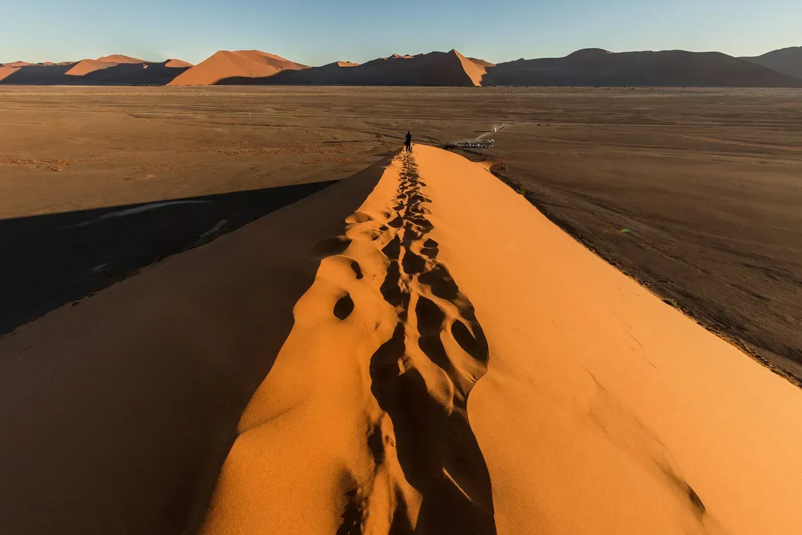 Footprints trail up a dune crest to a solitary climber at first light
